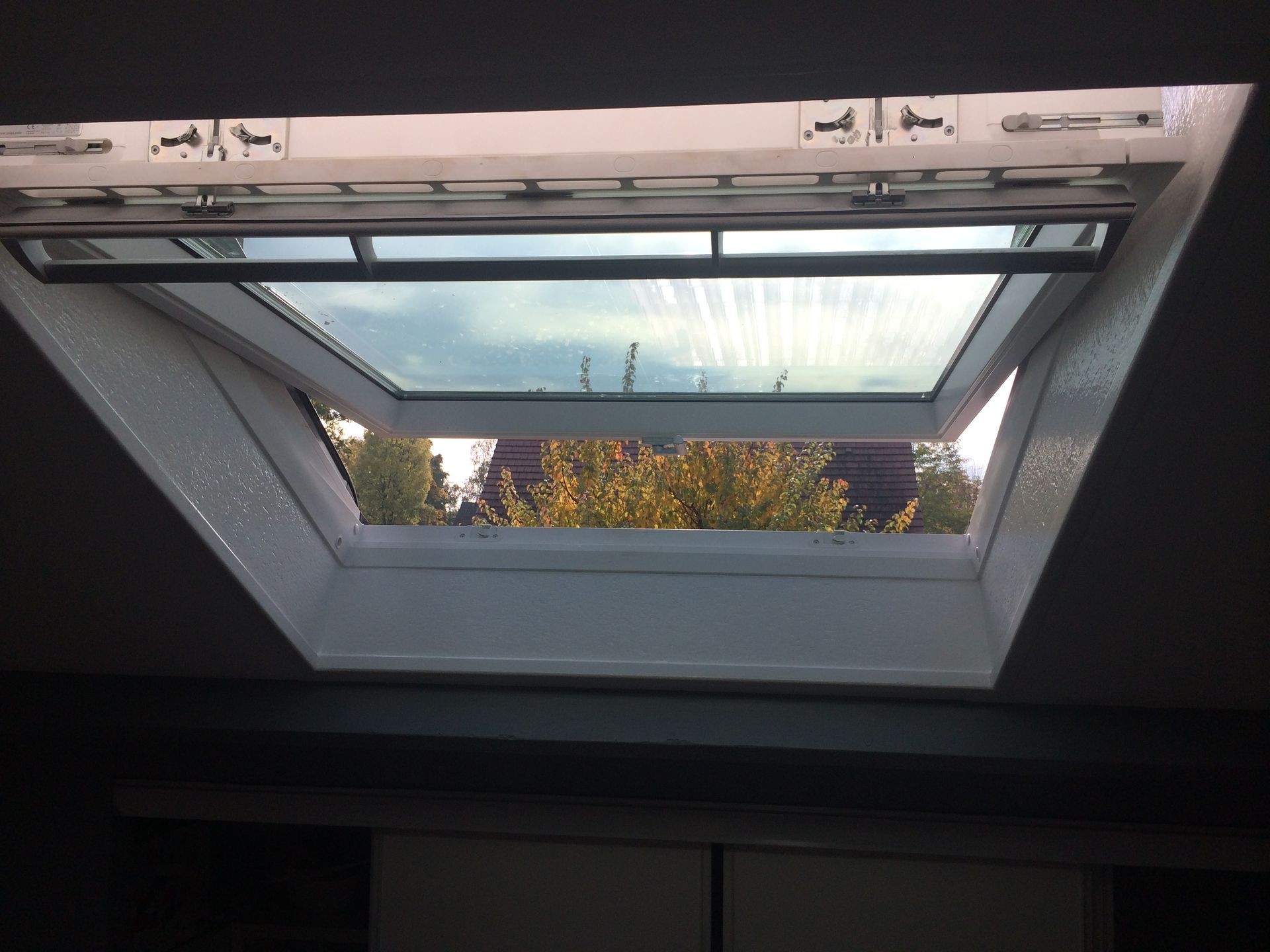 Open skylight window with a view of trees and a house roof in the background.