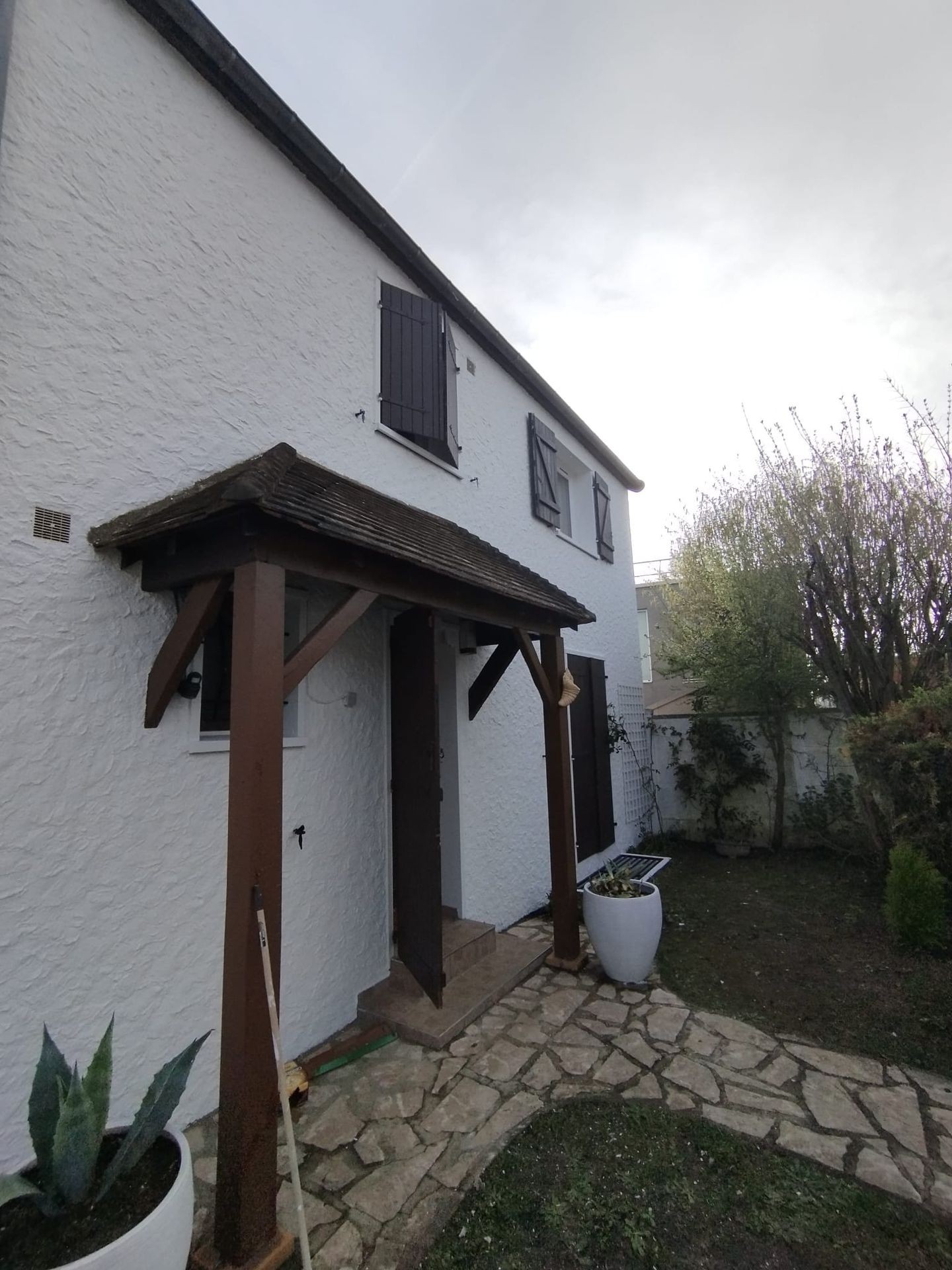 White two-story house with wooden shutters and stone path in small garden area.