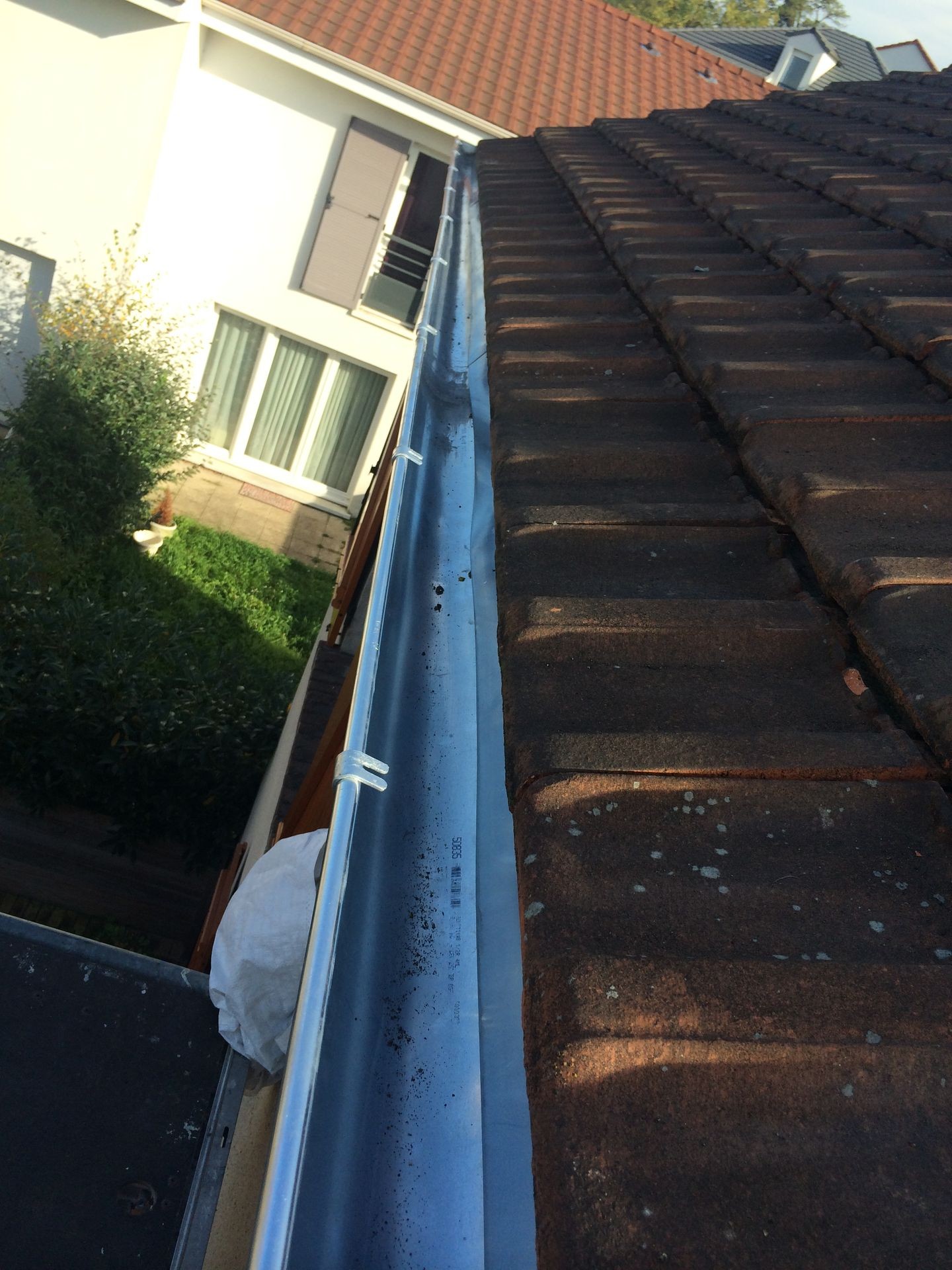 Roof with brown tiles and a clean gutter, next to a white building with windows.