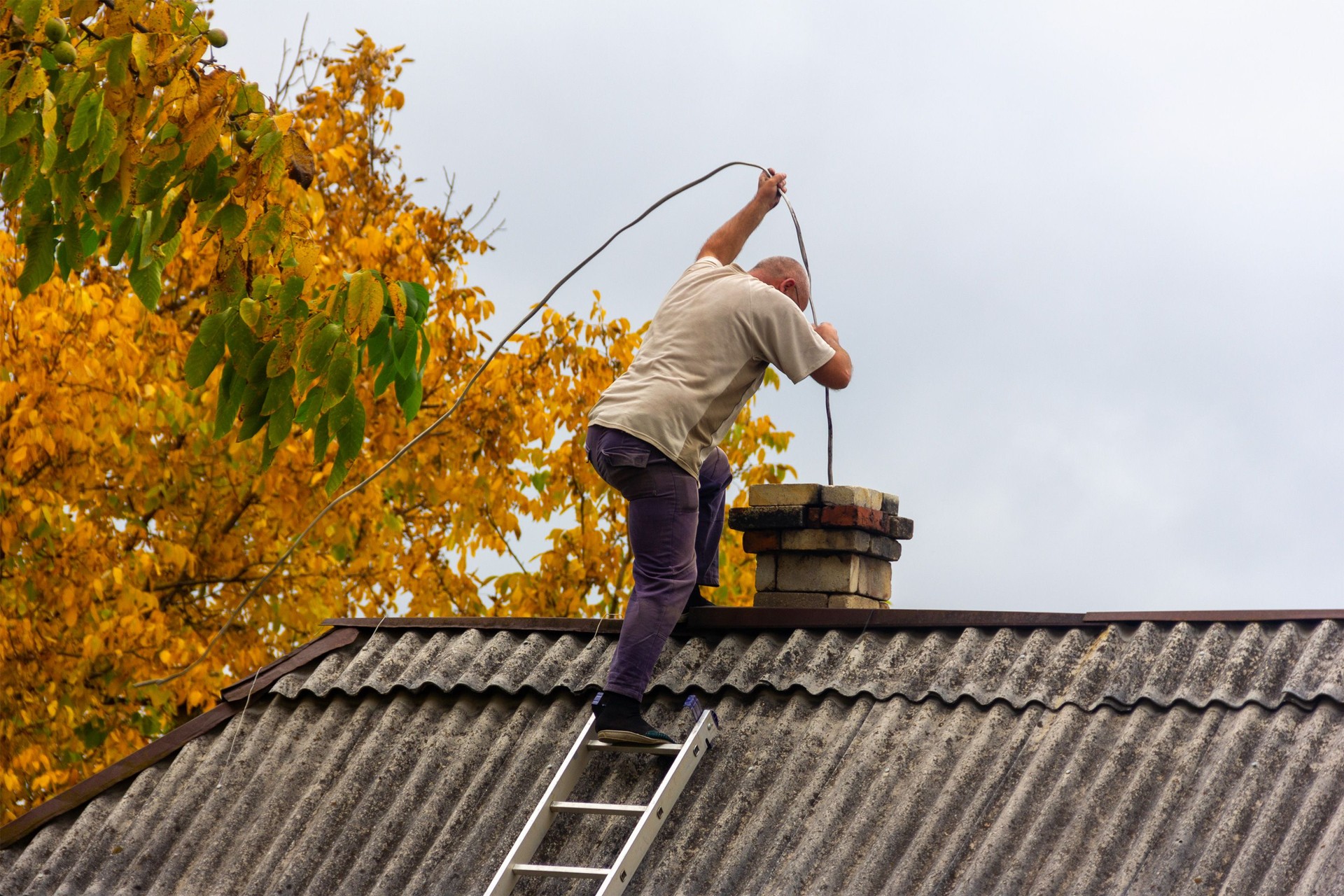 Un ramoneur masculin nettoie la cheminée de la suie sur le toit d’une maison de village, préparation pour la saison de chauffage